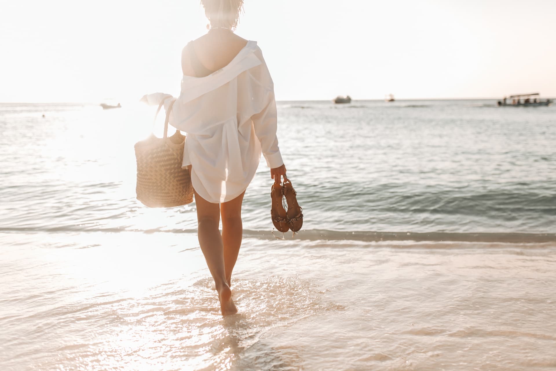 Mujer caminando por la orilla del mar con sandalias y bolso en las manos